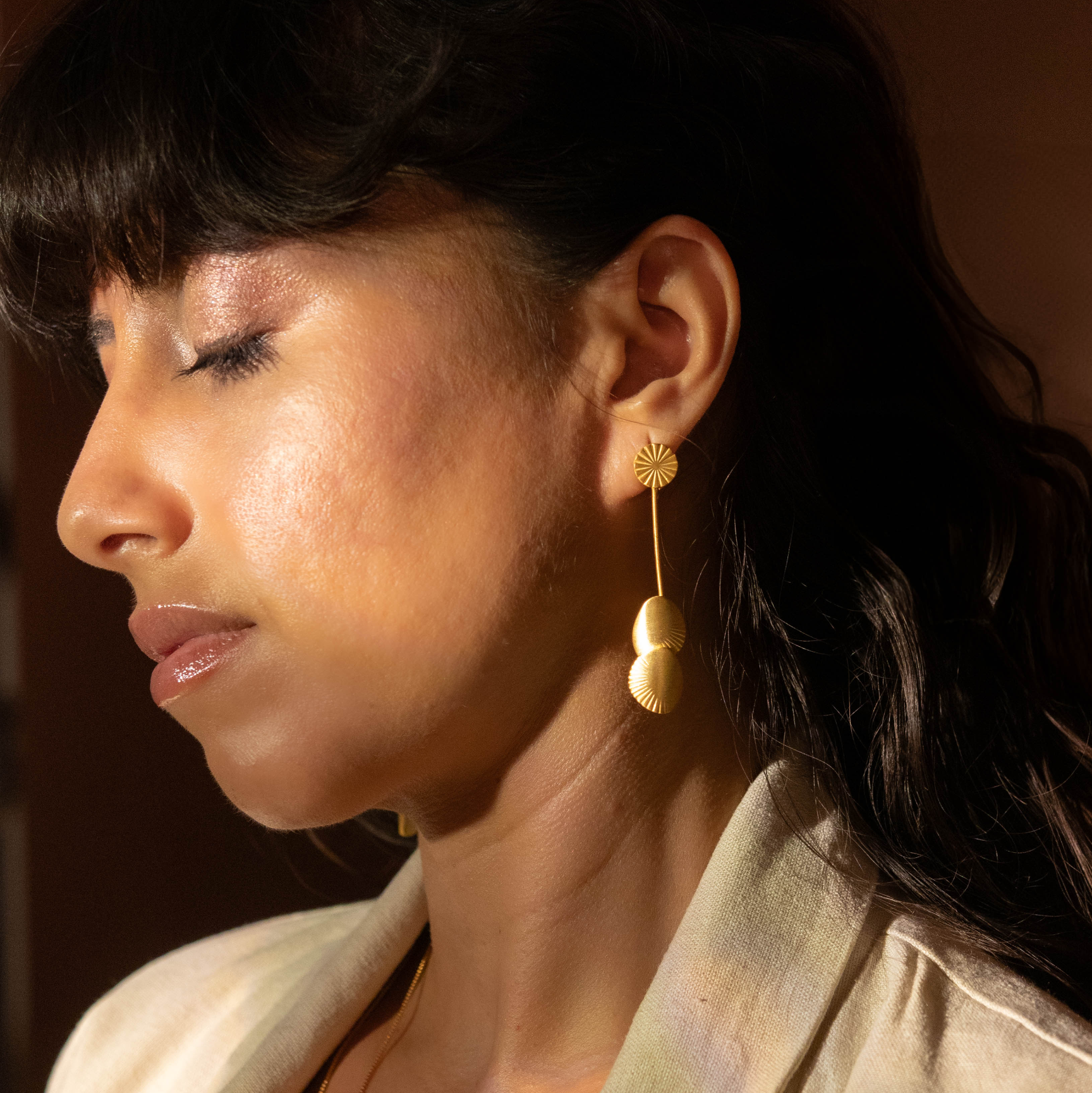 Woman wearing gold earrings and a necklace with a neutral background