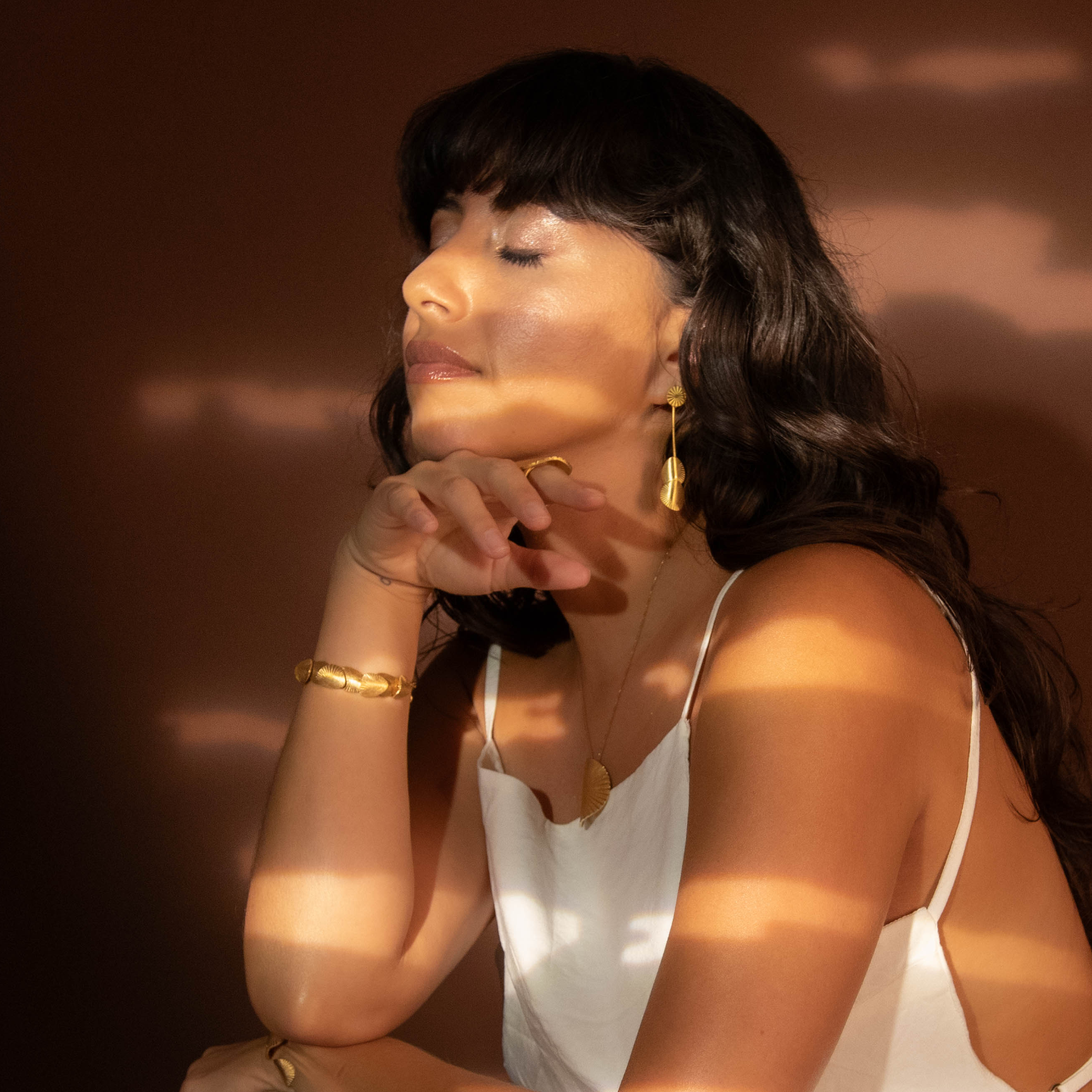Woman in a white dress sitting against a dark background with a warm glow