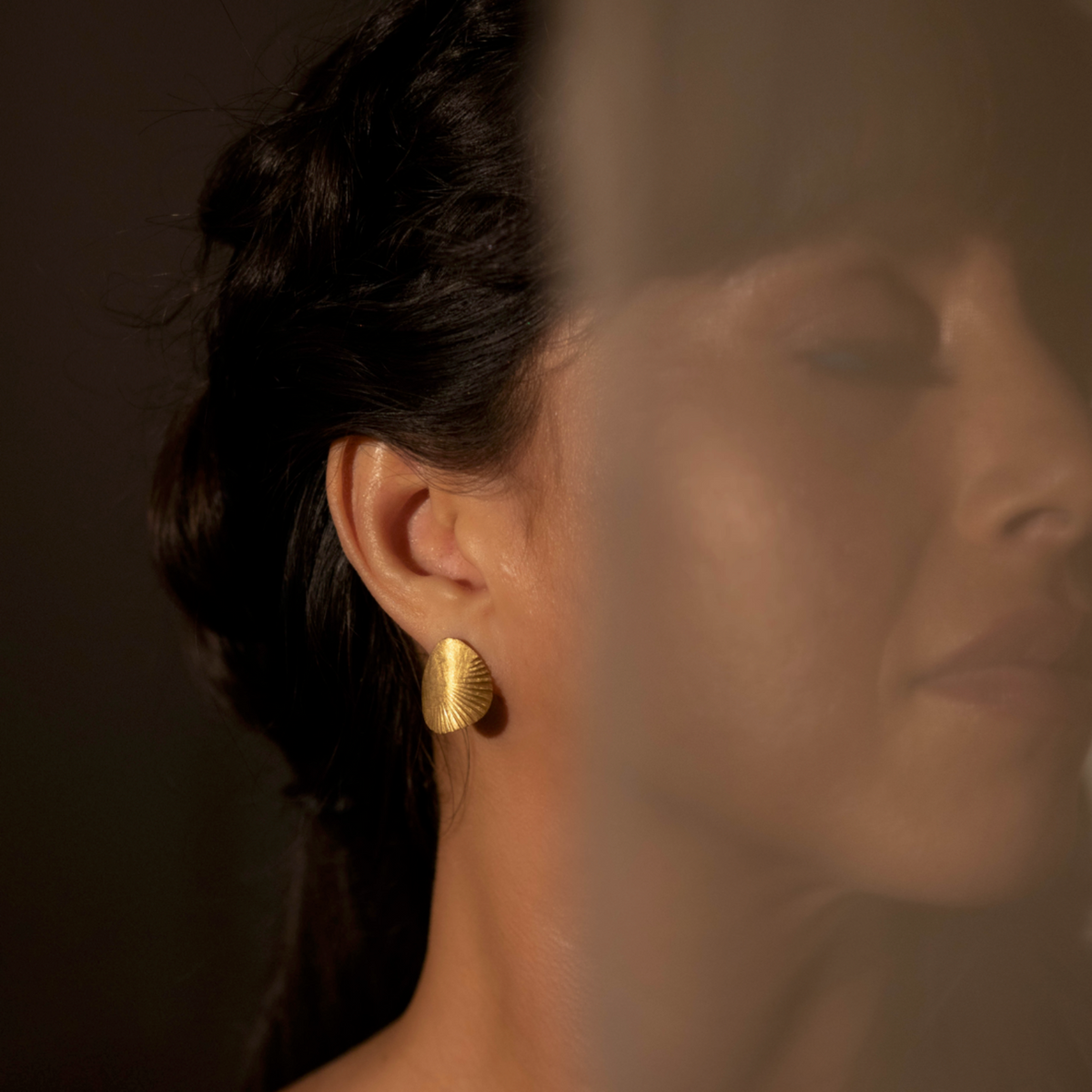 Close-up of a person wearing gold earrings with a blurred background