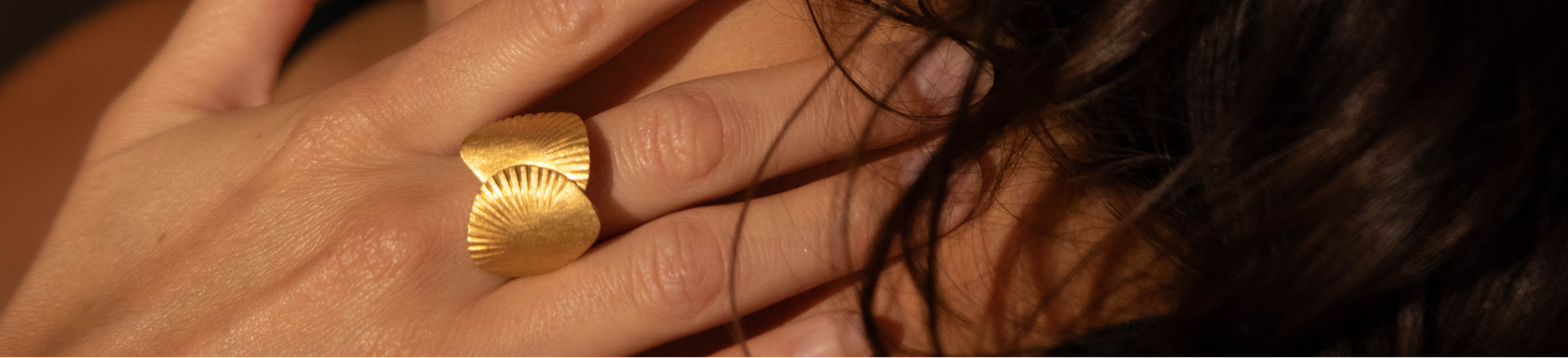 Close-up of a woman wearing gold earrings and a ring with a dark background