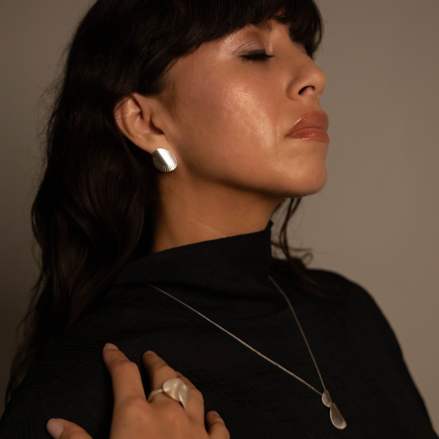 Woman wearing a black turtleneck with a necklace against a neutral background