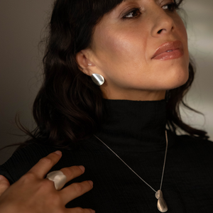 Woman wearing a black turtleneck with a necklace and earrings, against a neutral background.